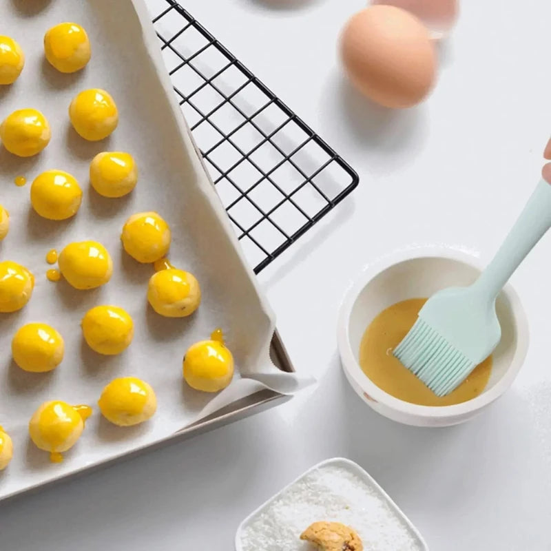 Baking process with yellow spherical treats on a tray, eggs, and a brush with a bowl of liquid.